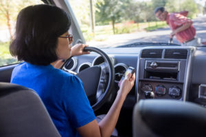 Distracted Driver texting while man crosses street in front of their car