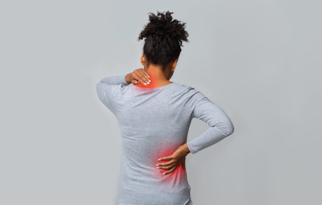 Back view of african woman rubbing her inflamed neck and back in pain after an accident, grey background