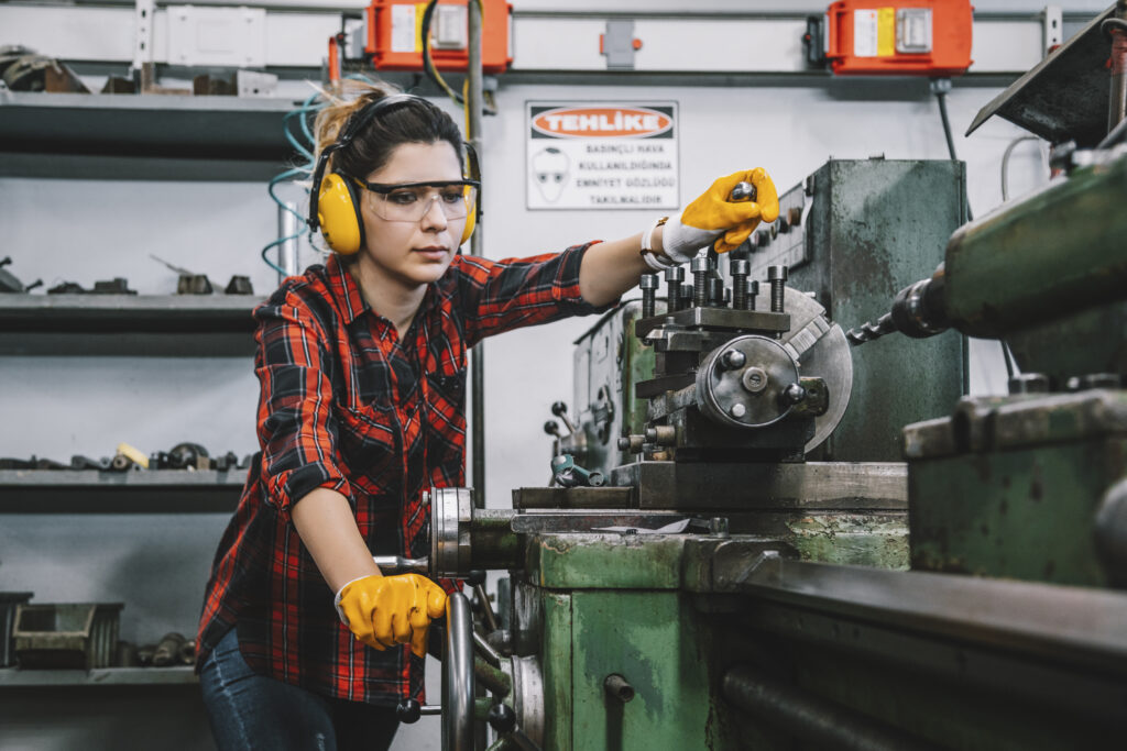 Portrait of hard working female industry technical worker or engineer woman confident serious face turner standing works on automatic universal cnc vertical milling machine for production of metal structures in an industrial manufacturing factory company.