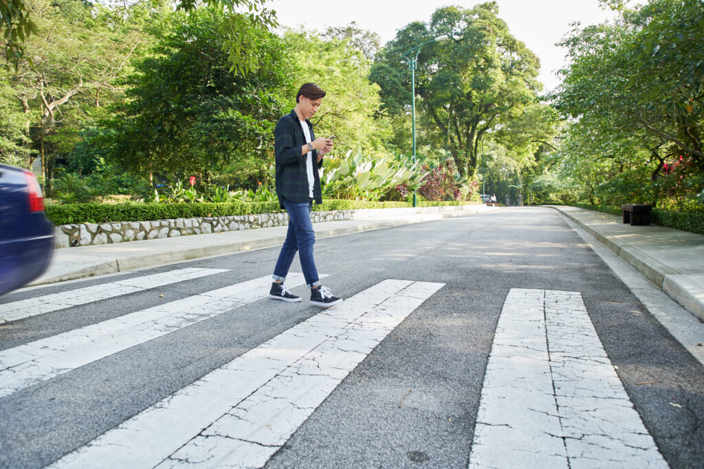 man crossing the street at a pedestrian crossing and looking his cellphone