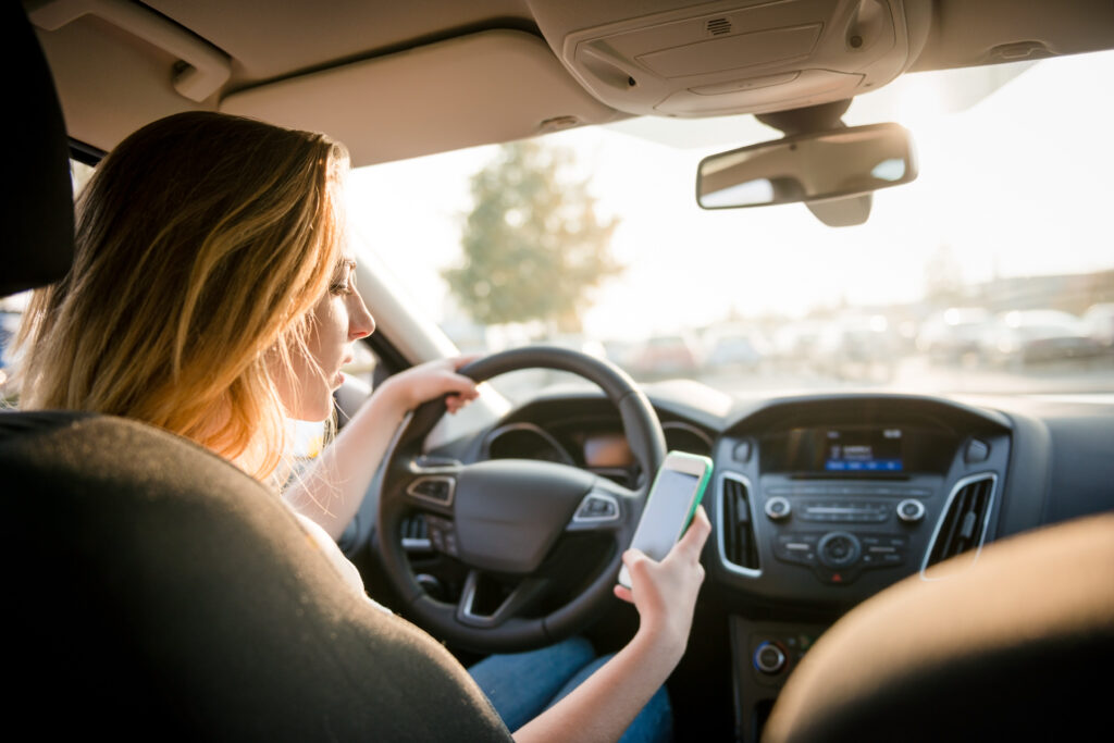 Young woman looking to her smartphone, texting while driving the car - distracted driving