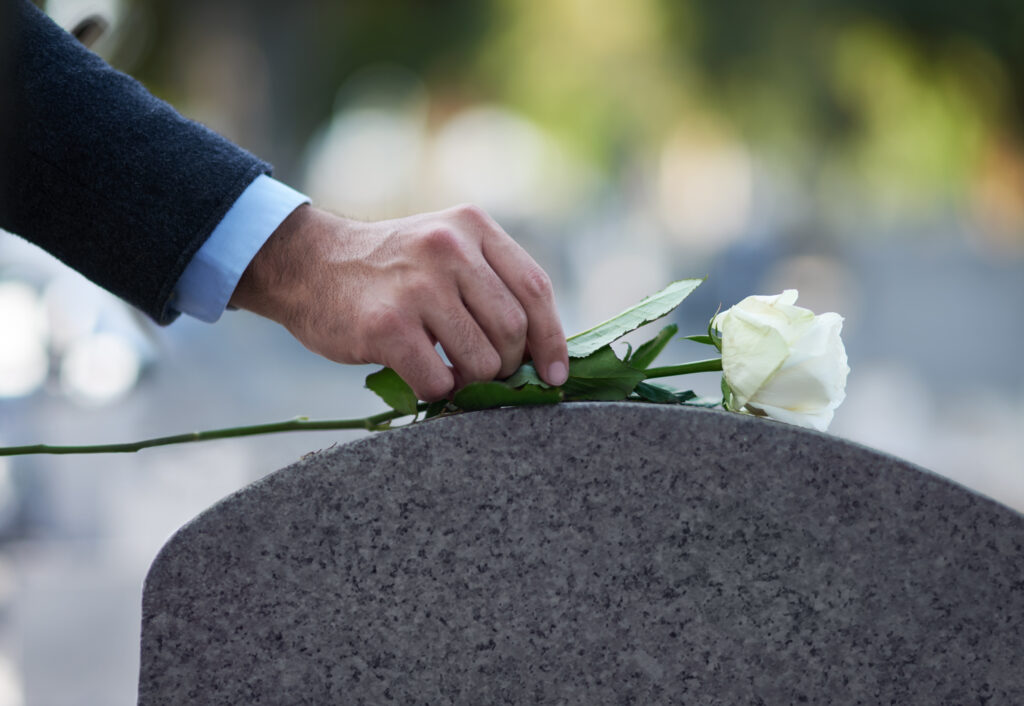 Cropped shot of a man placing a white rose on a grave of the victim of a wrongful death, greenville wrongful death