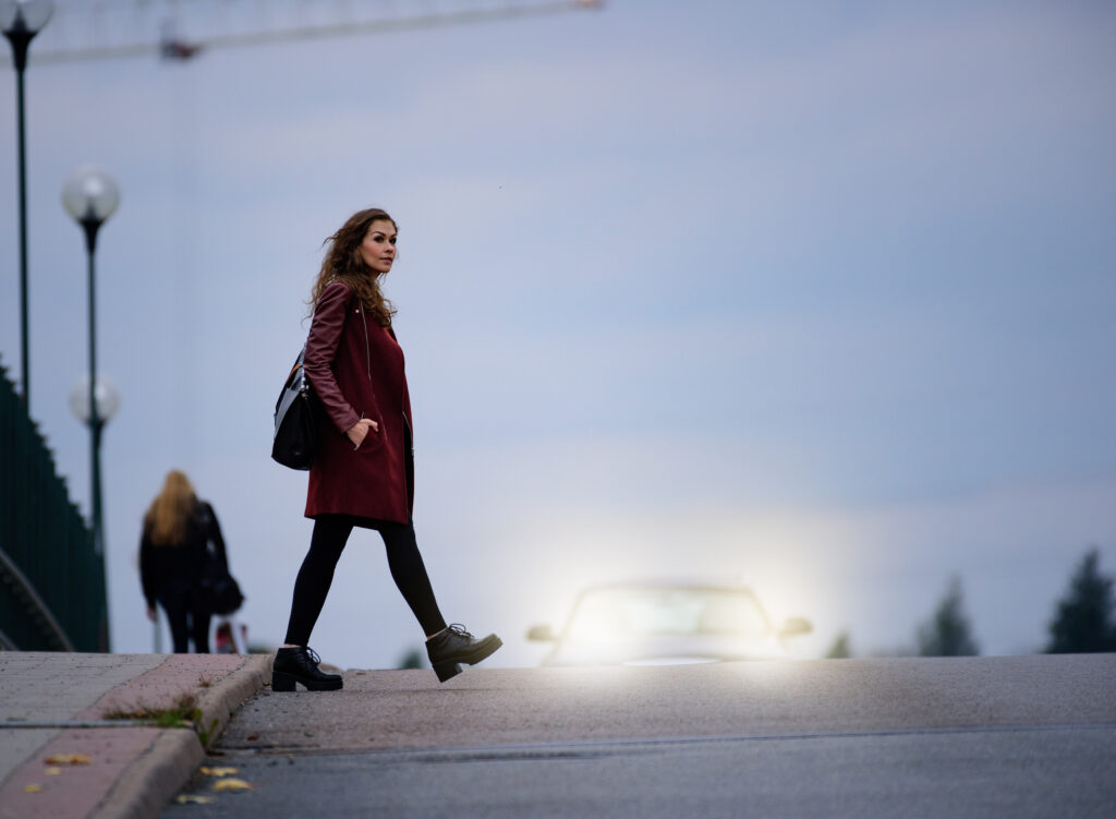 Woman crossing road dark bridge, car in background, pedestrian accident scene