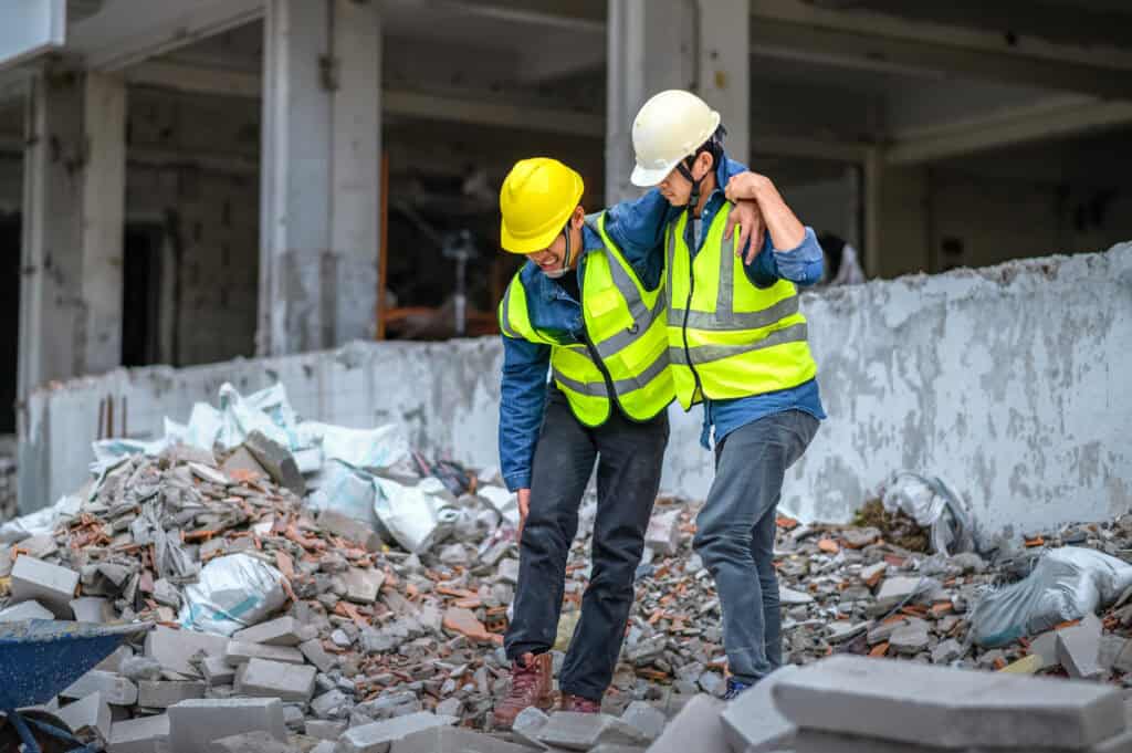 Los supervisores de construcción o ingenieros ayudan a los trabajadores de la construcción que tienen lesiones en las rodillas y las piernas, causadas por accidentes en el sitio de construcción. Tema de compensación de trabajadores
