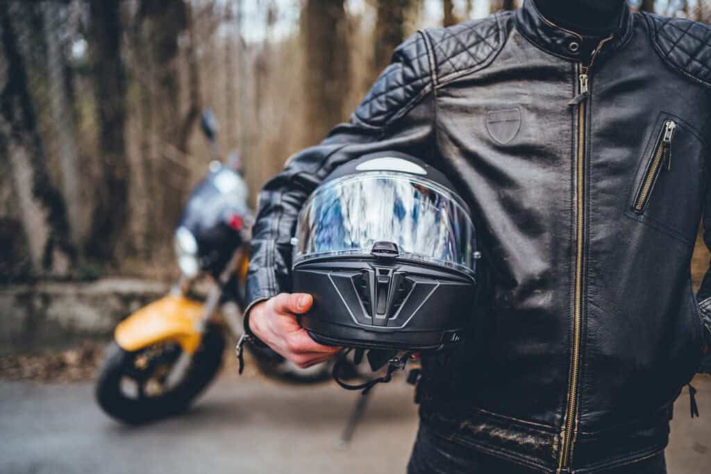 A motorcyclist holds his helmet as he stands in front of his motorcycle while preparing for a ride.